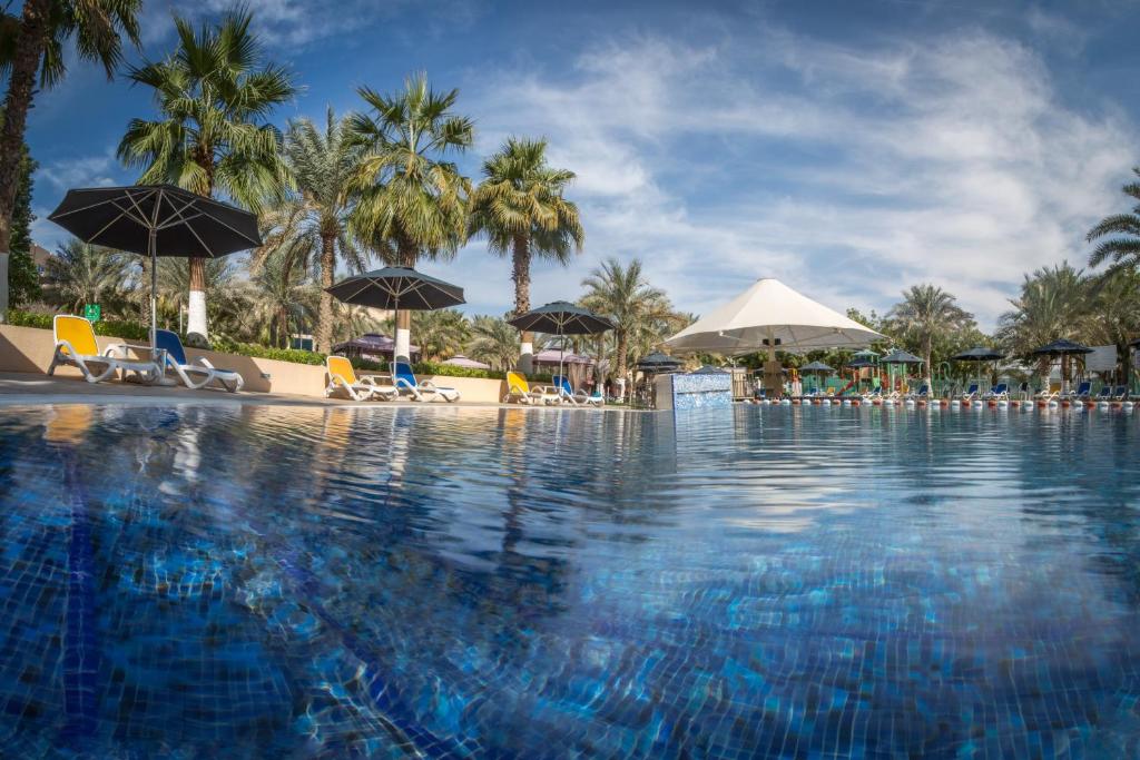 a large swimming pool with chairs and umbrellas at Metropolitan Al Mafraq Hotel in Abu Dhabi
