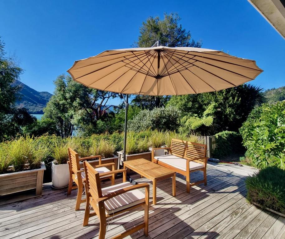 drewniany stół i krzesła z parasolem na tarasie w obiekcie Pukenui Paradise - Havelock Holiday Home w mieście Havelock