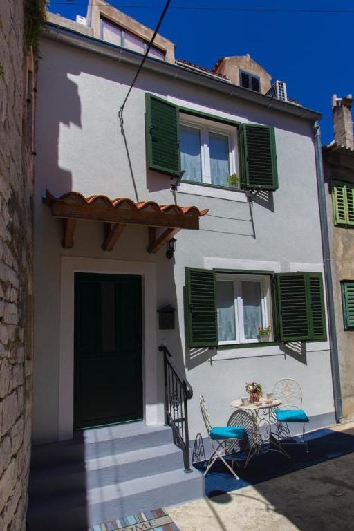 a white building with green shuttered windows and a table at Capitans House in Šibenik
