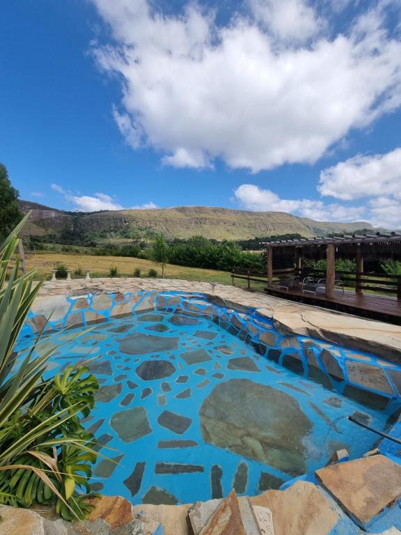 a pool with blue water with a mountain in the background at Chalés Encantos da Serra in Carrancas