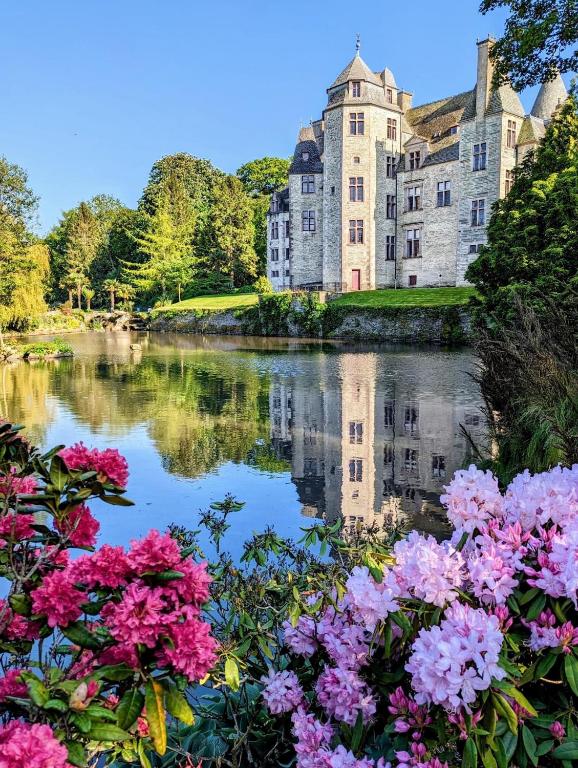 a castle with flowers in front of a body of water at Maison Village de La Verrerie in Cherbourg en Cotentin