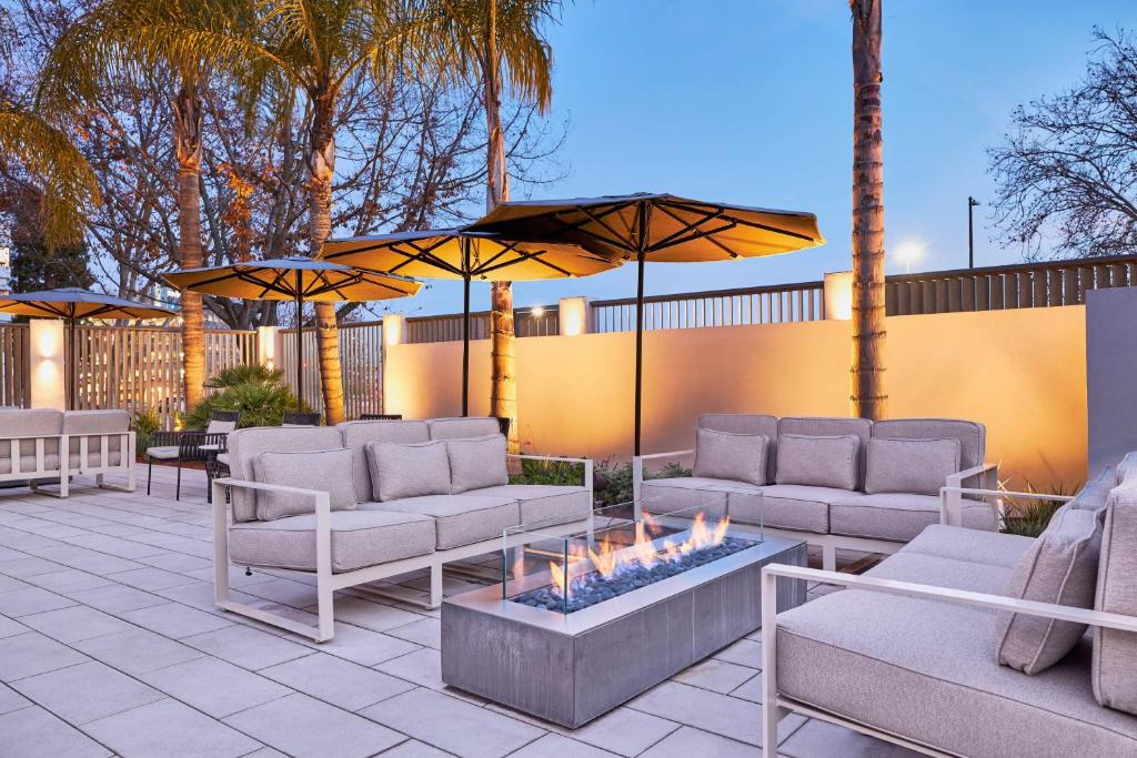 eine Terrasse mit Sofas und eine Feuerstelle mit Sonnenschirmen in der Unterkunft AC Hotel by Marriott Pleasanton in Pleasanton