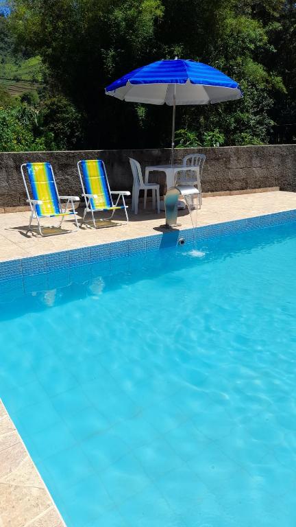 duas cadeiras e um guarda-sol junto a uma piscina em Canto do Pássaro Aconcheg em São Bento do Sapucaí