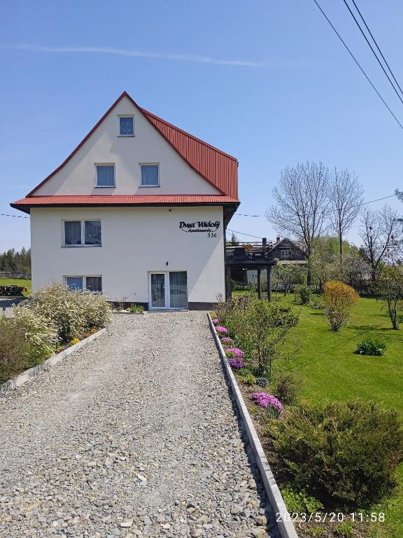 a white house with a red roof on a gravel road at Dwa Widoki Apartamenty in Zubrzyca Górna