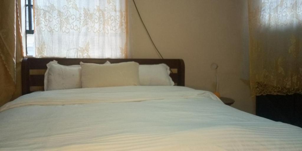uma cama com lençóis brancos e almofadas num quarto em The Buckingham Palace Nahashon Kimemia Studio em Nairobi