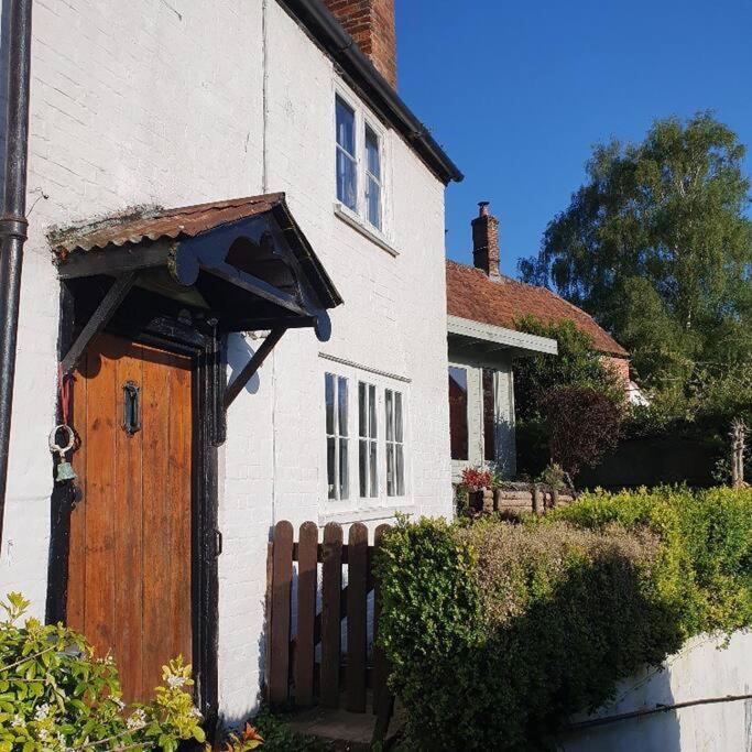 une maison blanche avec une porte en bois et une clôture dans l'établissement Priory Cottage, à Westbury