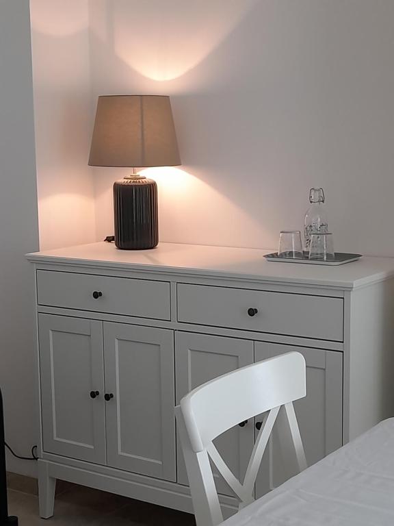 een wit dressoir met een lamp en een stoel bij APE BIANCA - Appartamento Lavanda in Colico