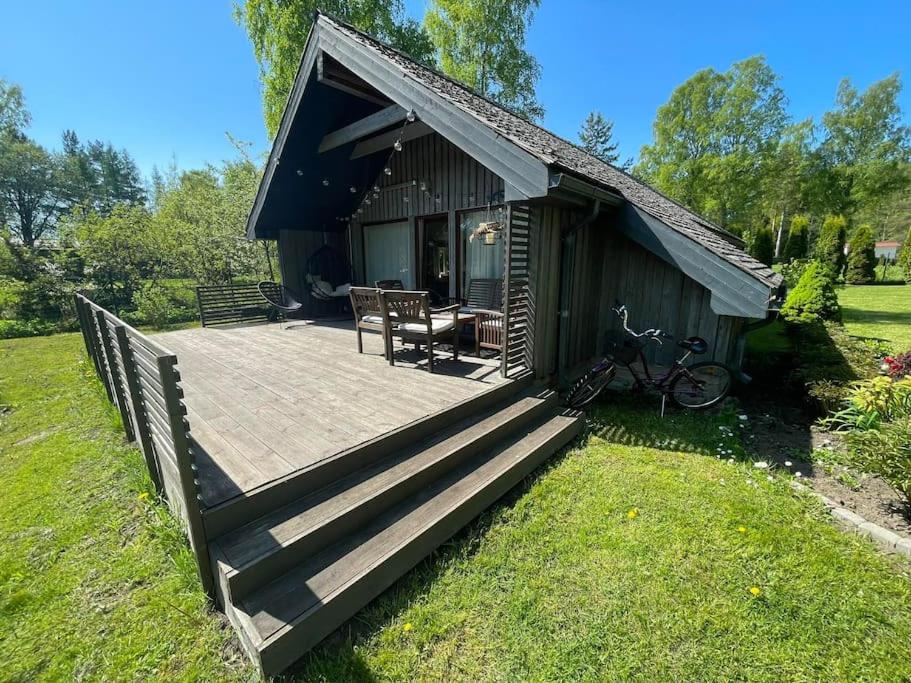 a cabin with a wooden deck in the grass at Sea Side house (70m2) Lejas Ziediņi in Plieņciems
