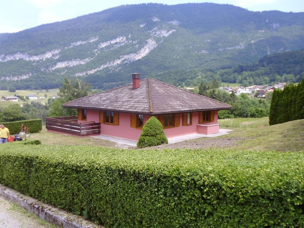 una pequeña casa rosa en un campo con un seto en La Mosa - Villa ai Prati di Cavedago, nel comprensorio del parco Adamello-Brenta, en Cavedago