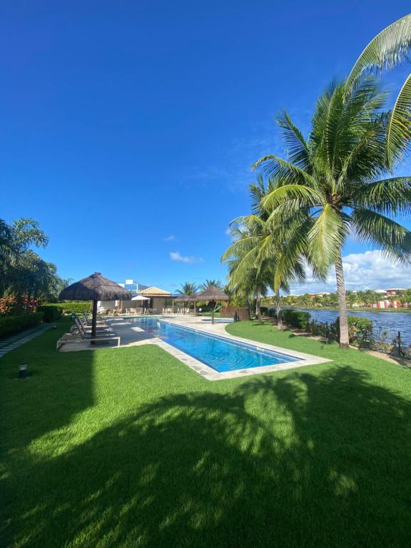 a resort swimming pool with a palm tree and water at Refúgio na Praia do Forte in Praia do Forte