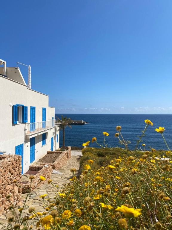 a building and a field of yellow flowers next to the ocean at Bilocale Punta Basano in Marettimo