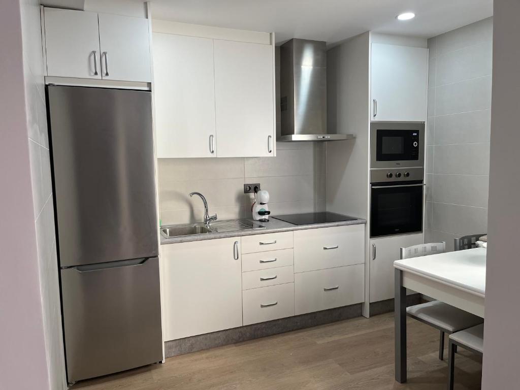 uma cozinha com armários brancos e um frigorífico de aço inoxidável em Apartamento puerto em A Guarda
