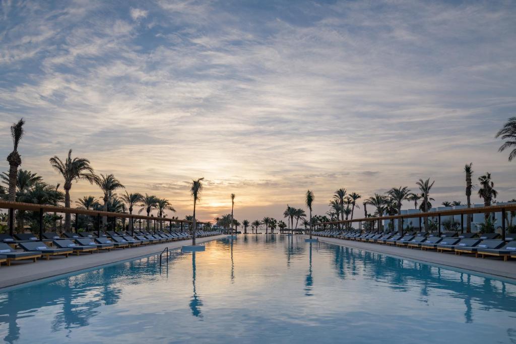 a pool with chairs and palm trees at sunset at Serry Beach Resort in Hurghada
