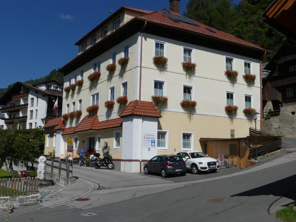 un grand bâtiment blanc avec des voitures garées devant lui dans l'établissement Hotel Kirchenwirt, à Bad Kleinkirchheim