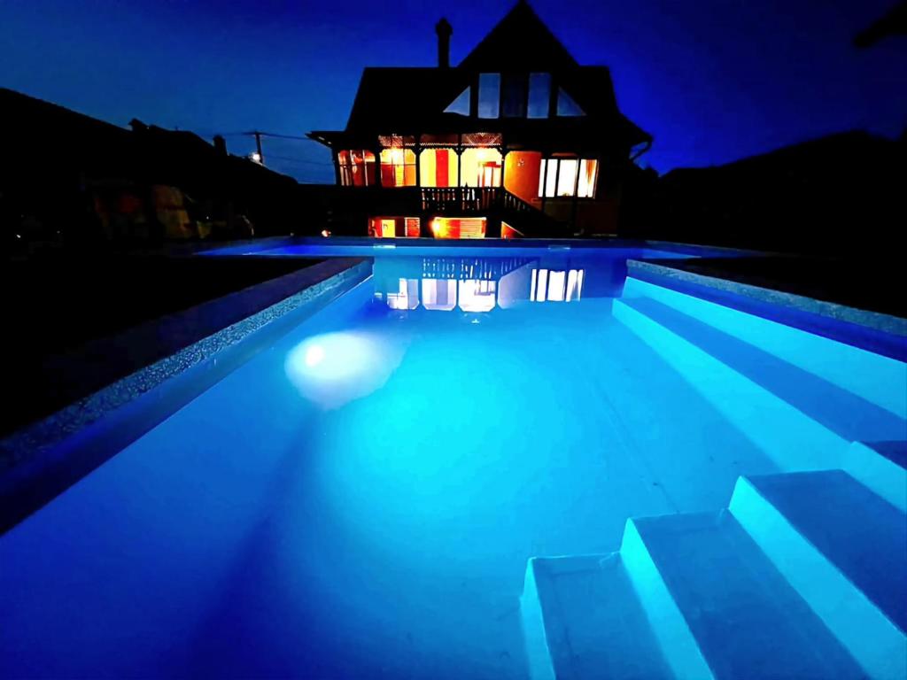 a swimming pool at night with a house in the background at VILA COCA Sibiu in Sălişte