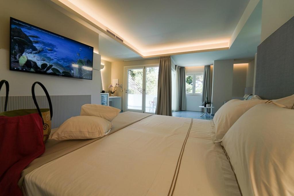 a bedroom with two beds and a tv on the wall at Hotel Village Eden in Capo Vaticano