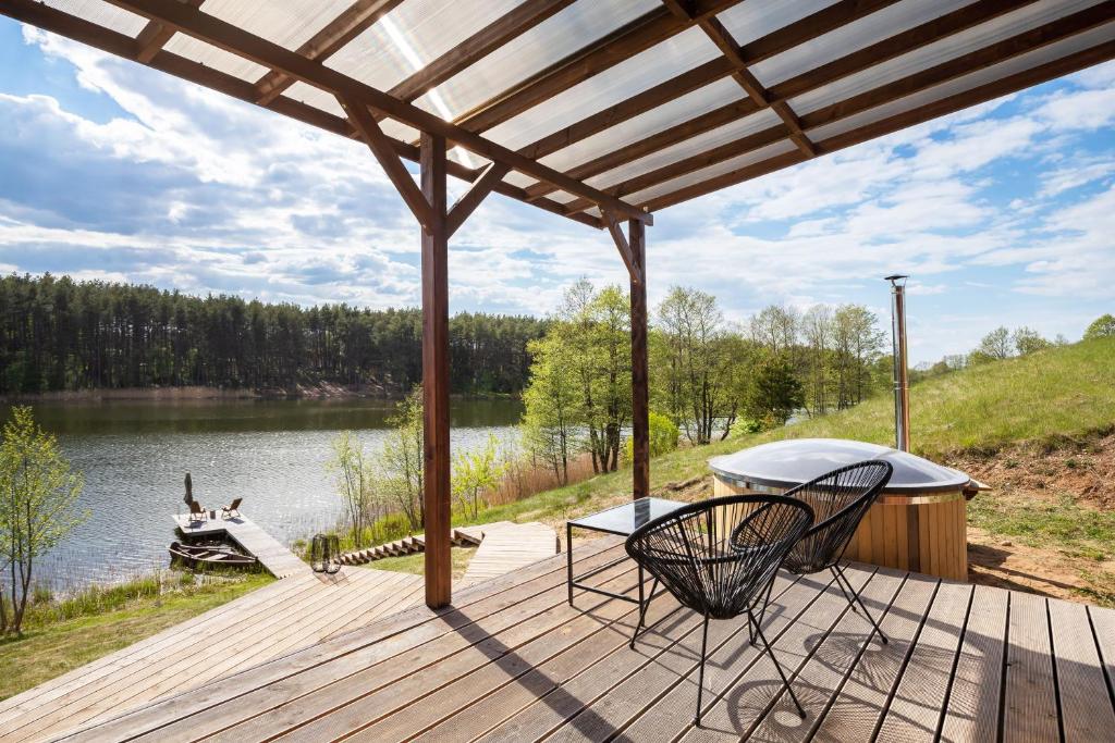 une terrasse en bois avec des chaises et un bateau sur un lac dans l'établissement Pineplace twins NIDA, à Žaugėdai