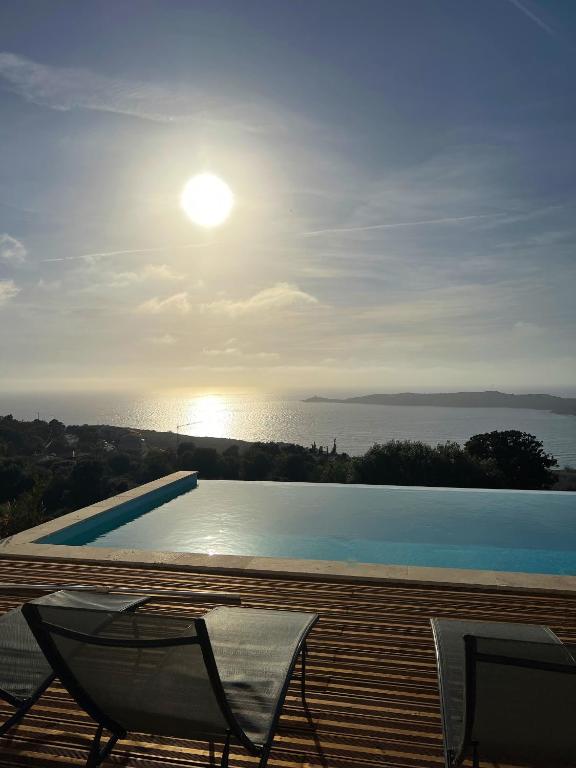 - une piscine avec 2 chaises et le soleil dans le ciel dans l'établissement Appartement 140M2 villa cargèse, à Cargèse
