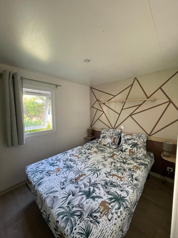 1 dormitorio con 1 cama con colcha de flores y ventana en Mobil-Home au pied du Luberon, en La Roque-d'Anthéron