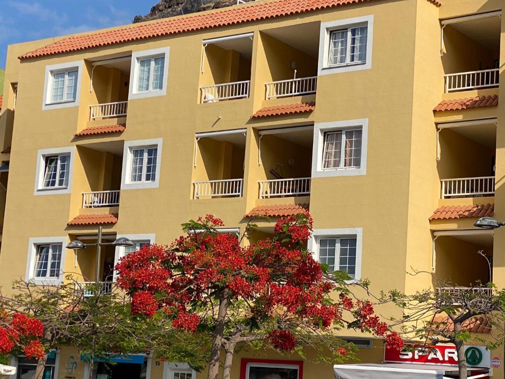 a yellow building with red flowering trees in front of it at Tazacortes Beach and also Luz y Mar apartments in Puerto