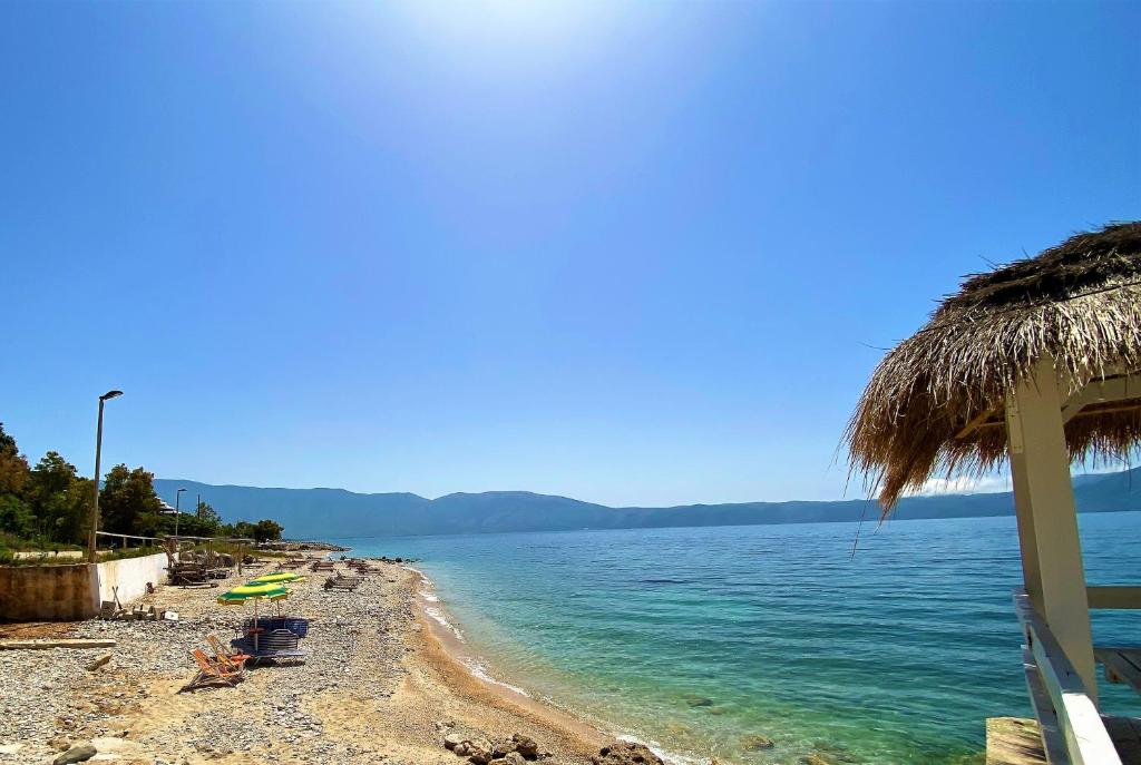 una playa con una cabaña de paja y el océano en Ramo's Hilltop Retreat with Kitchenette and Patio - 1st en Vlorë