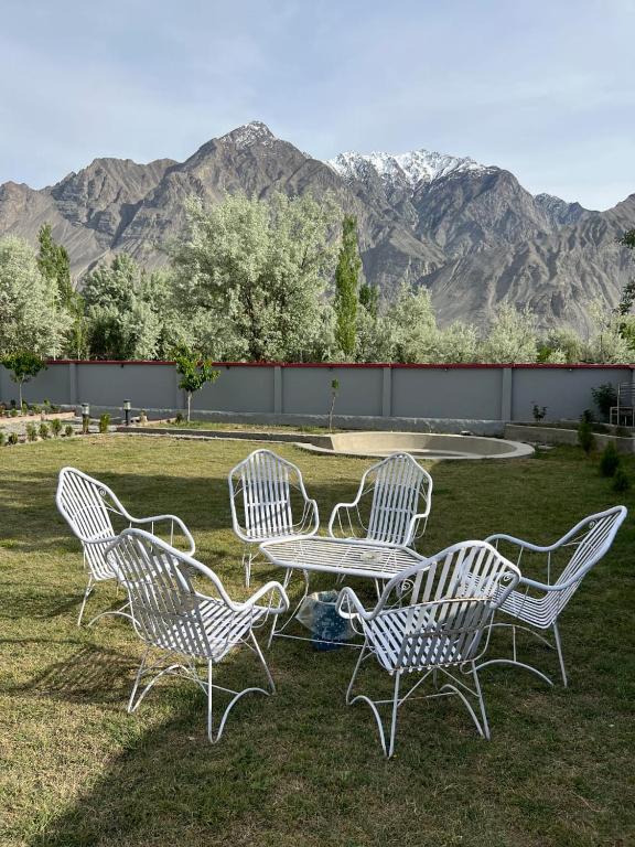 four white chairs and a table in a field with mountains at Royal Resort Skardu in Skardu