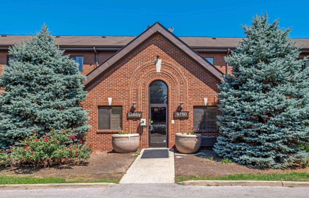 a brick building with two pine trees in front of it at Extended Stay America Select Suites - Indianapolis - North - Carmel in Carmel