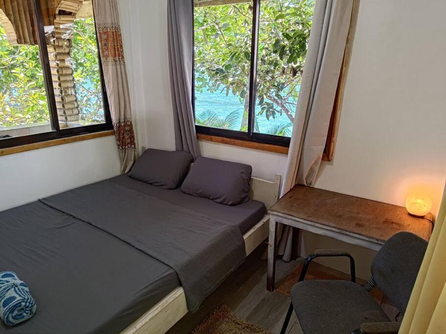 a bedroom with a bed and a desk and two windows at Treehouse Front Beach Bacong in Bacong
