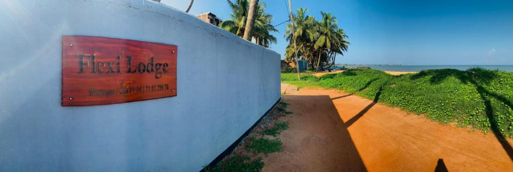 ein Schild an einer Wand neben einer unbefestigten Straße in der Unterkunft Flexi Lodge in Negombo