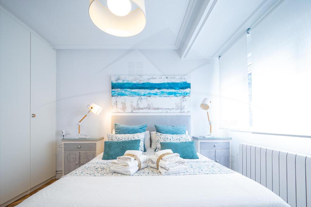 a white bedroom with a bed with blue pillows at Playa Apartamento Frente al mar in Gijón