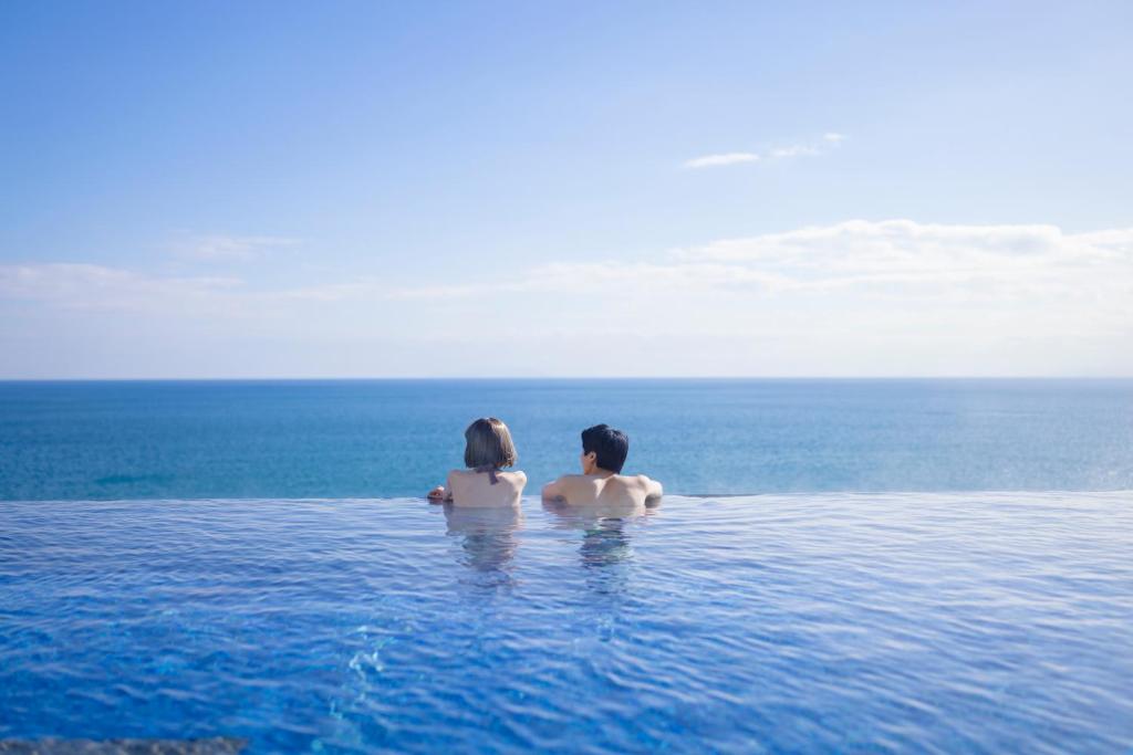 a man and woman sitting in a swimming pool in the ocean at Oiso Prince Hotel in Oiso