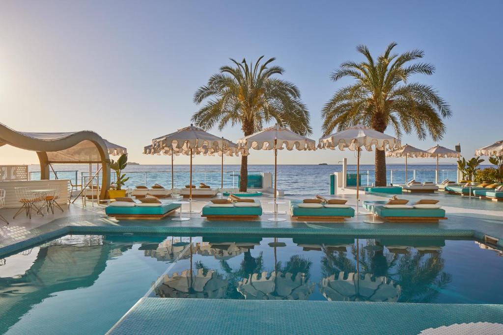 um resort com piscina, palmeiras e oceano em Dorado Ibiza - Adults Only em Playa d'en Bossa