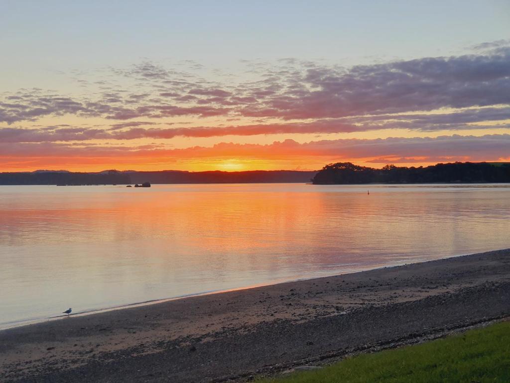 una puesta de sol sobre un cuerpo de agua con una playa en Makuri Bay Hideaway en Purerua