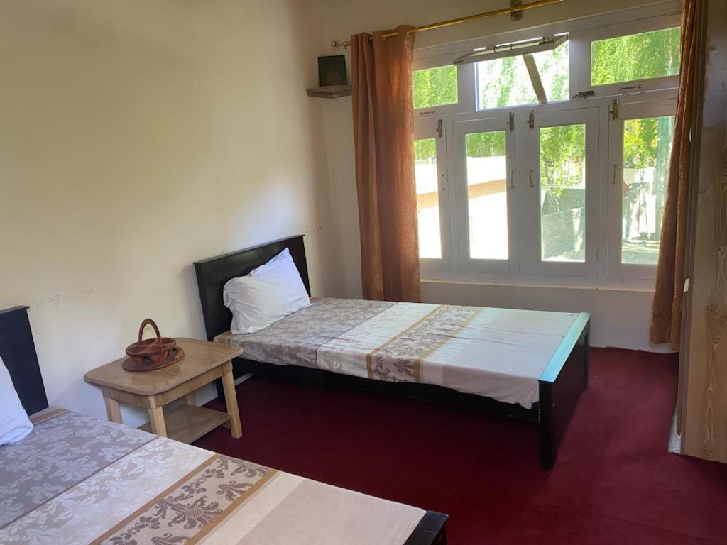 a room with two beds and a table and windows at Moon Light Guest House Khaplu in Khaplu