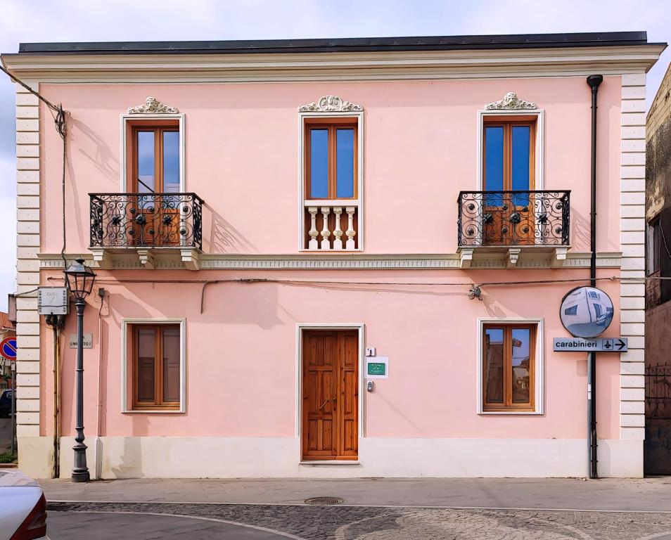 a pink building with windows and balconies on a street at La Residenza B&B in Giba