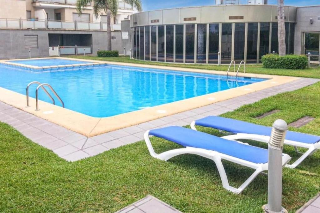a swimming pool with two blue lounge chairs in the grass at Moderno apartamento en Oliva Nova golf & MET in Oliva