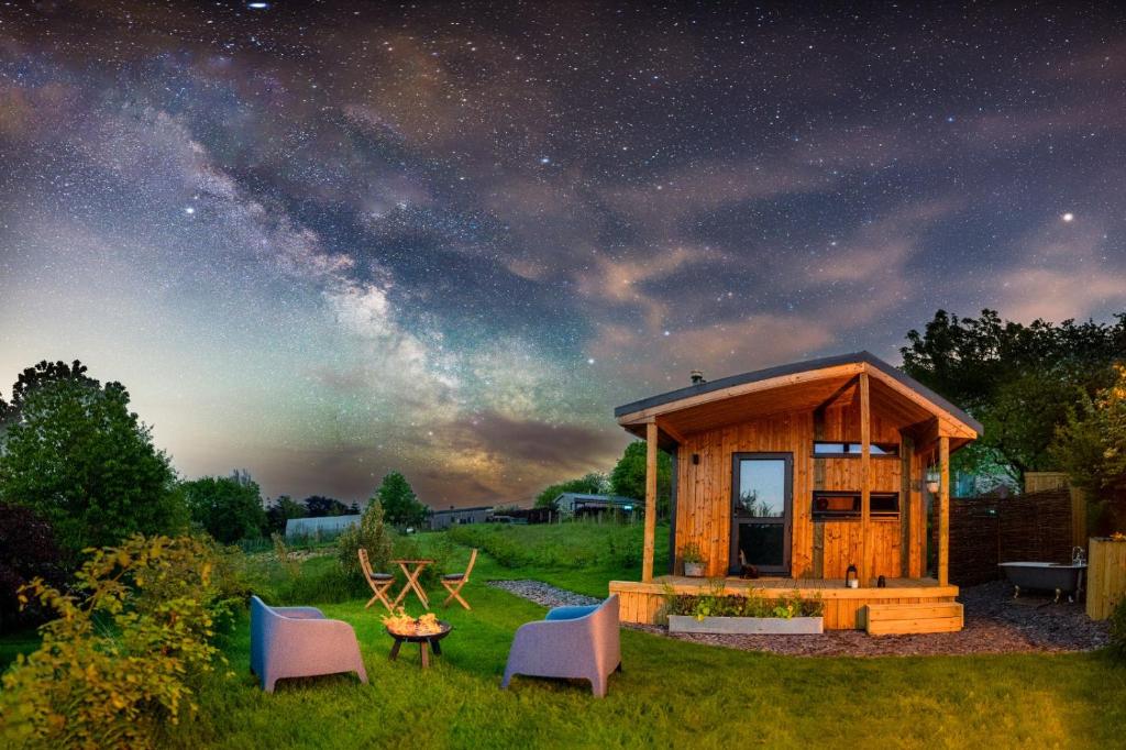 a small wooden cabin with chairs and a table in a field at Luxury Glamping Cabin with Outdoor Bath on Cornish Flower Farm in Truro