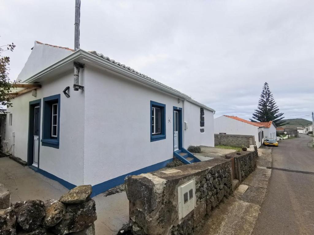 una piccola casa bianca con finestre blu e un muro in pietra di Casa da Emilie a Santa Cruz da Graciosa