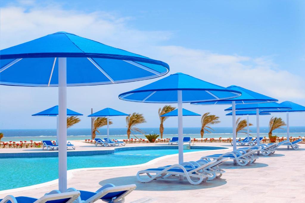 Pickalbatros Villaggio Aqua Park - Portofino Marsa Alam في مرسى علم: مجموعة من المظلات والكراسي الزرقاء بجانب المسبح