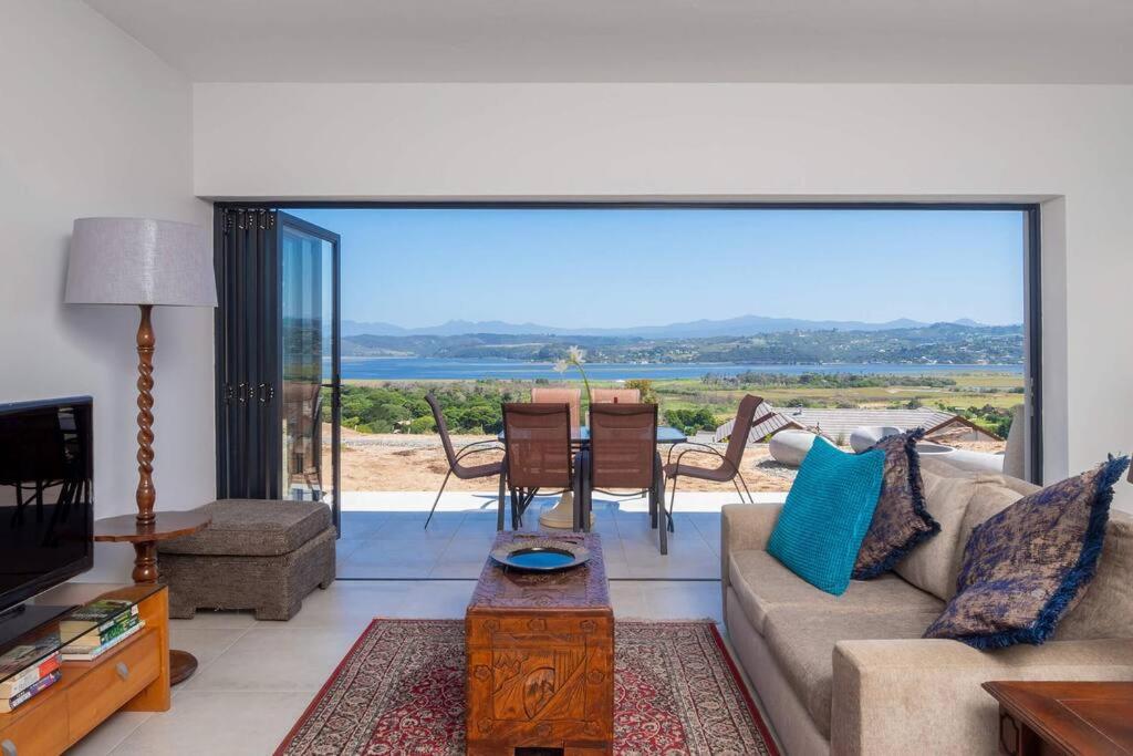 a living room with a couch and a table and a large window at Heron's View - lagoon views and solar power @Lake Brenton, Knysna in Knysna