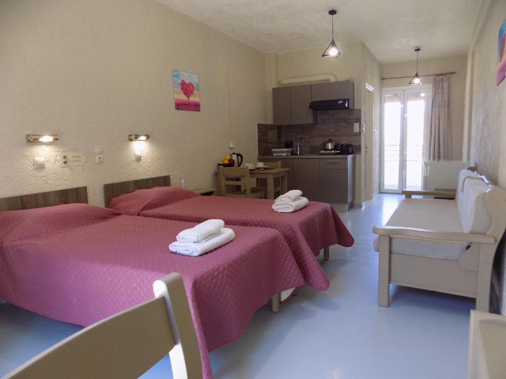 a bedroom with two beds with pink sheets and a kitchen at Afrodite Spacious Apartments! in Ayia Evfimia