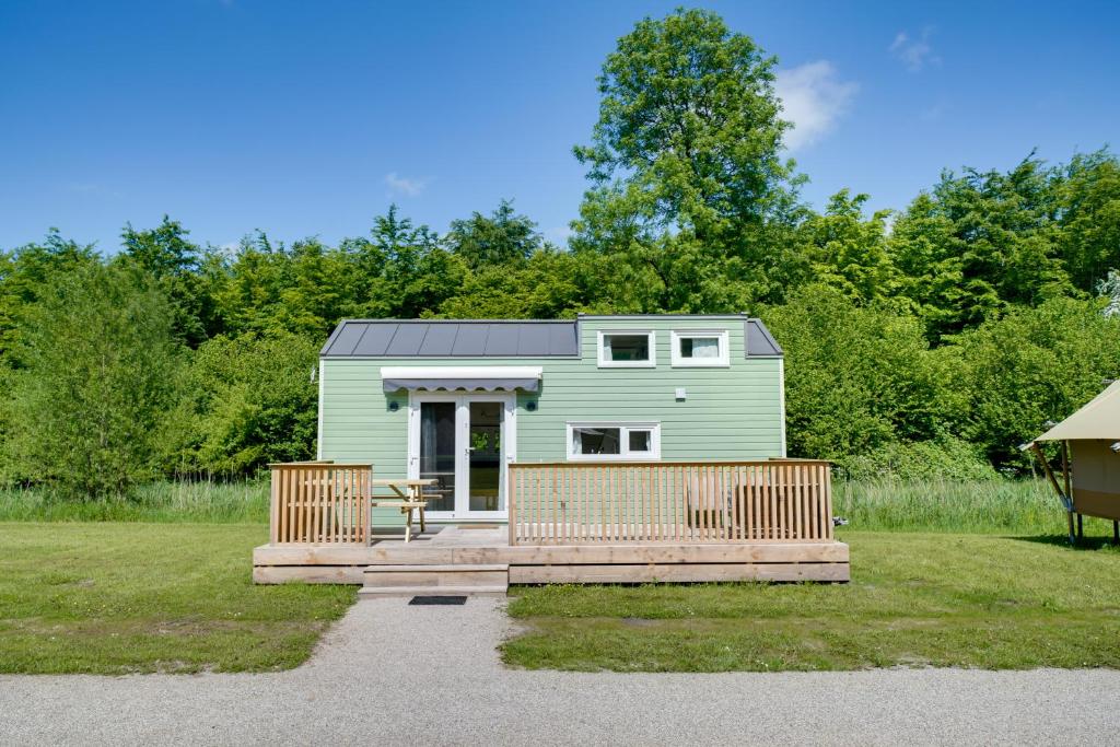 ein kleines grünes Haus mit einer Veranda im Hof in der Unterkunft Green Tiny House with shared pool in Zeewolde