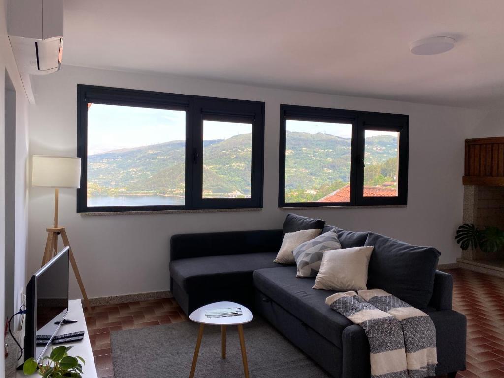 ein Wohnzimmer mit einem schwarzen Sofa und 3 Fenstern in der Unterkunft Casa Rodrigues in Terras de Bouro