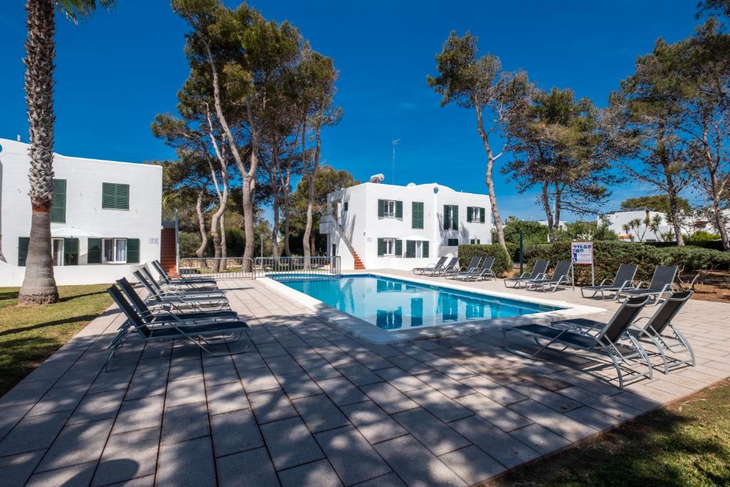 a pool with lounge chairs and a house in the background at Apartamentos Llebeig in Ciutadella