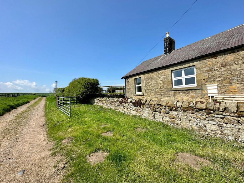 a stone house with a stone wall next to a field at Lonnon Cottage in Alnwick