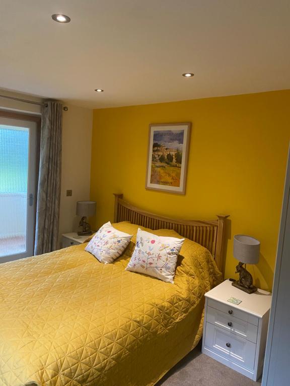 a yellow bedroom with a bed with two pillows at Otters End in Dilham