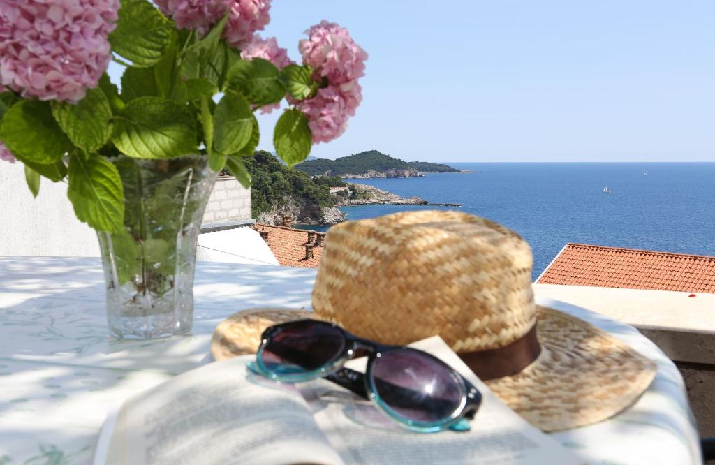 un chapeau et des lunettes de soleil assis sur une table avec un vase de fleurs dans l'établissement Rooms Cvetka, à Dubrovnik