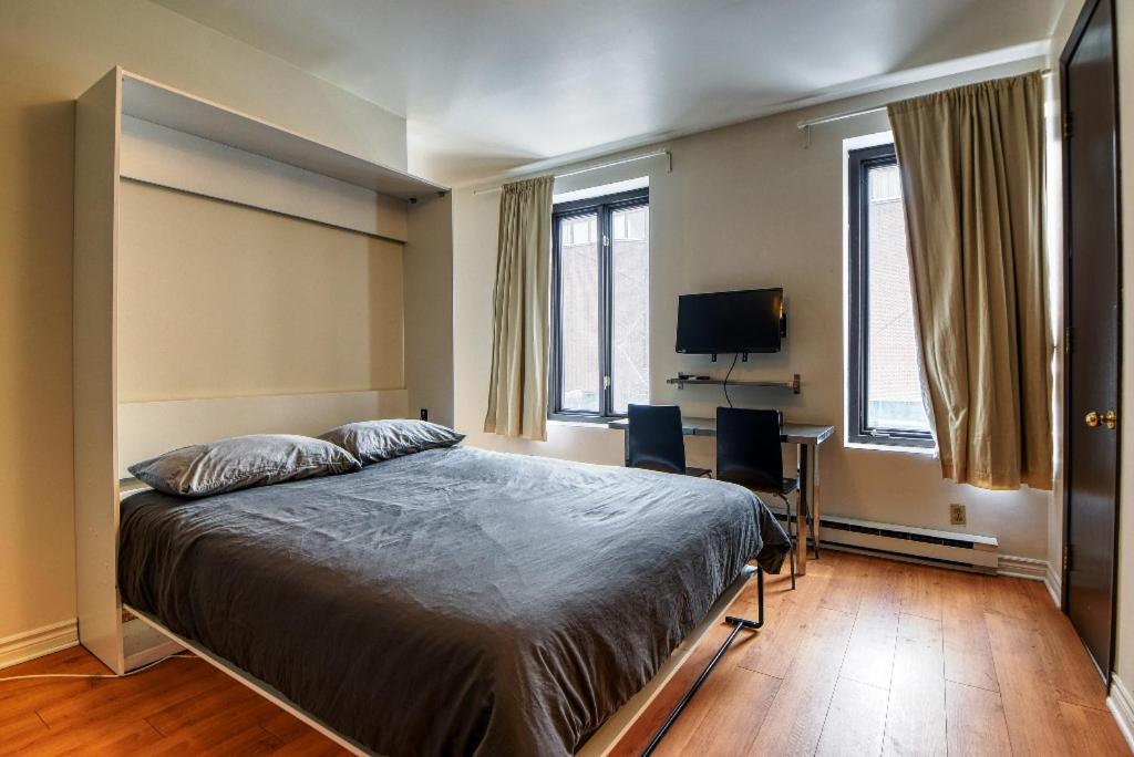 een slaapkamer met een bed en een bureau en twee ramen bij Studio Stays Downtown Montreal in Montreal