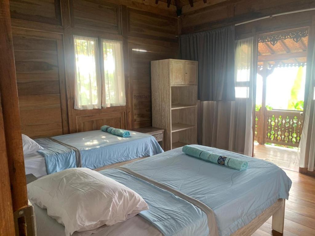 two beds in a room with wooden walls and windows at Villa Bakso Mentigi in Teluk Nara