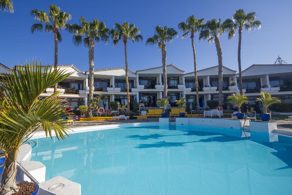 a swimming pool with palm trees in front of a hotel at Sunsuites Carolina & Collection in San Agustin